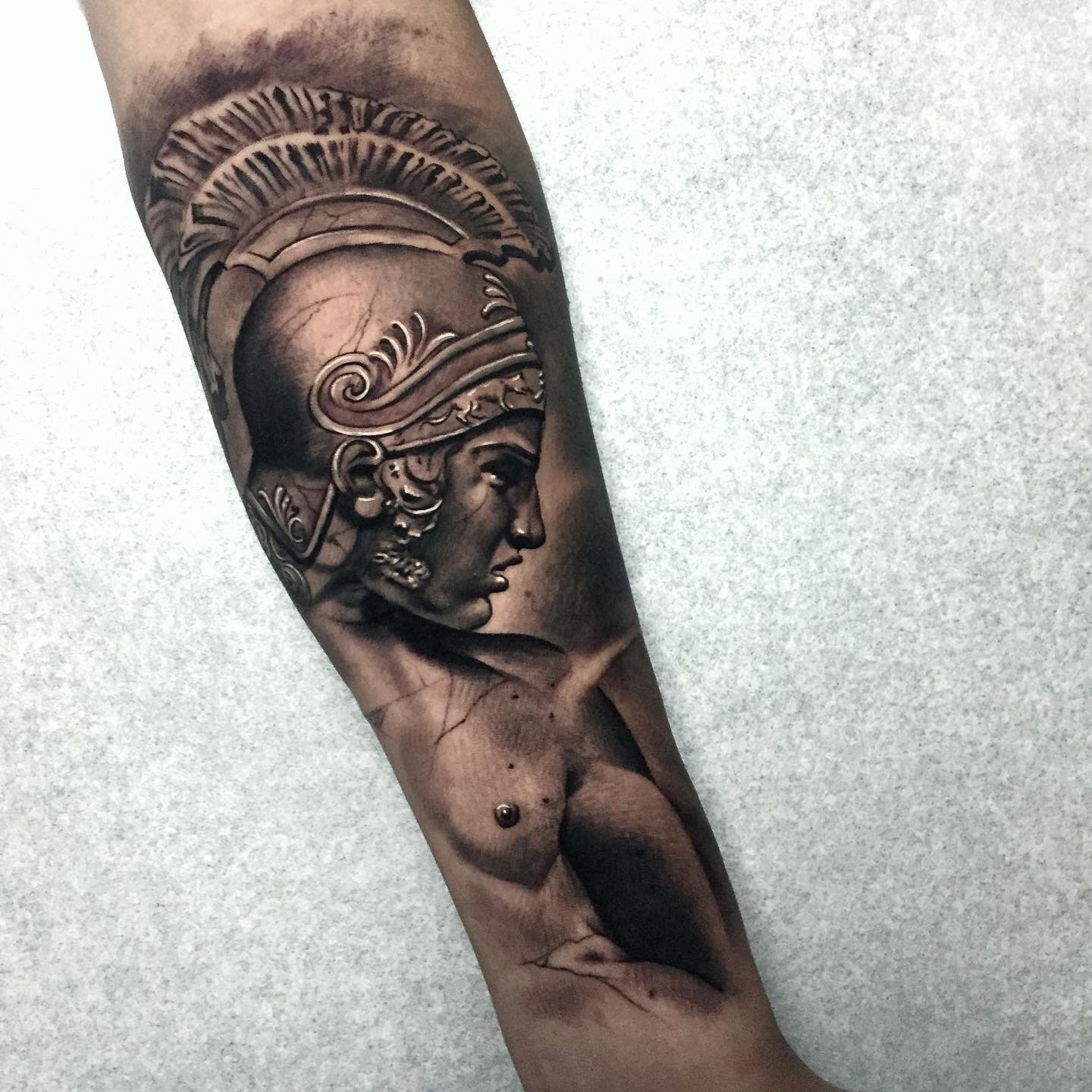 Greyscale tattoo of Achilles wearing a helmet on a forearm