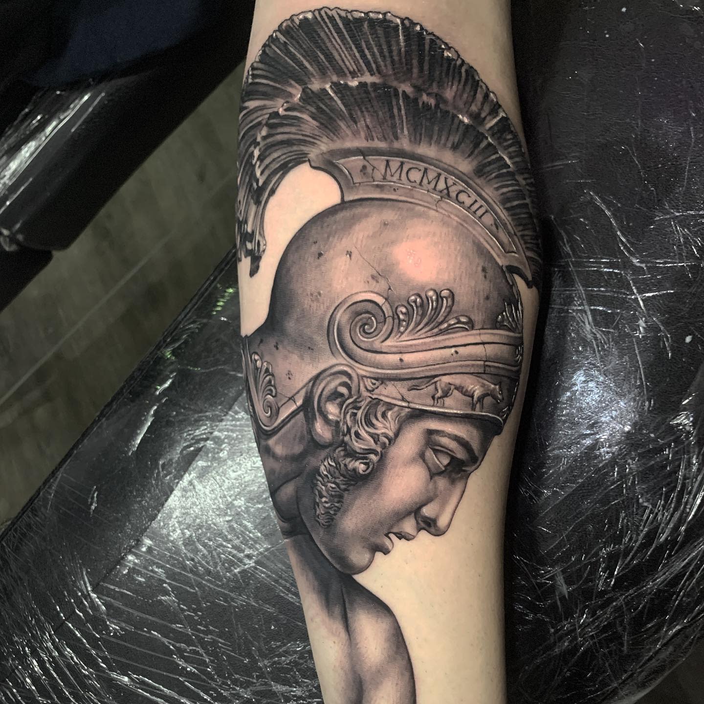 Tattoo of Achilles wearing a detailed helmet with Roman numerals on a forearm