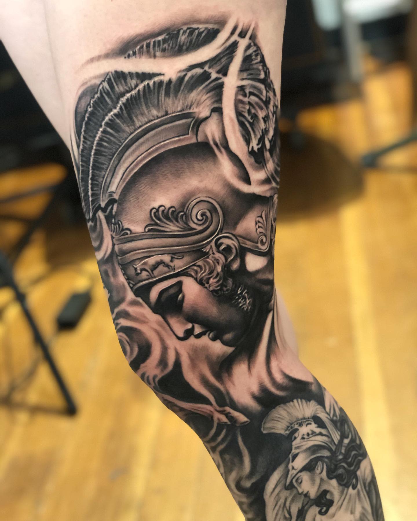 Detailed black-and-grey tattoo of a helmeted warrior Achilles on a leg