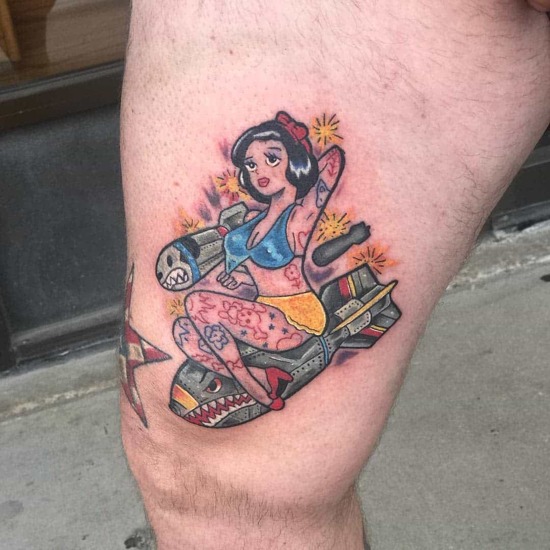 Tattoo of pin-up Snow White in retro style, riding a cartoon missile with a shark face on a thigh