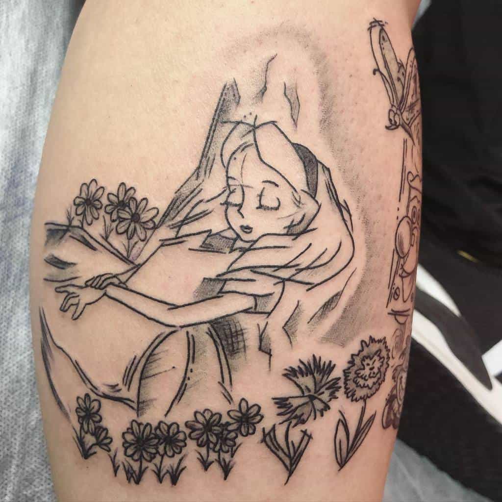 Black and white tattoo of Alice from Alice in Wonderland, surrounded by flowers, with a peaceful expression as she holds a book lying in tree