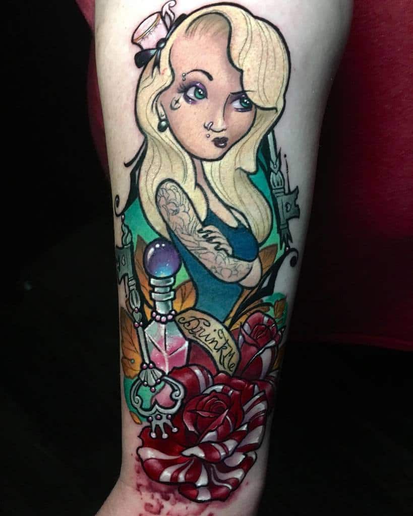 Colorful tattoo of a stylized Alice from Alice in Wonderland, surrounded by roses, a potion bottle labeled 'Drink Me,' and a heart key