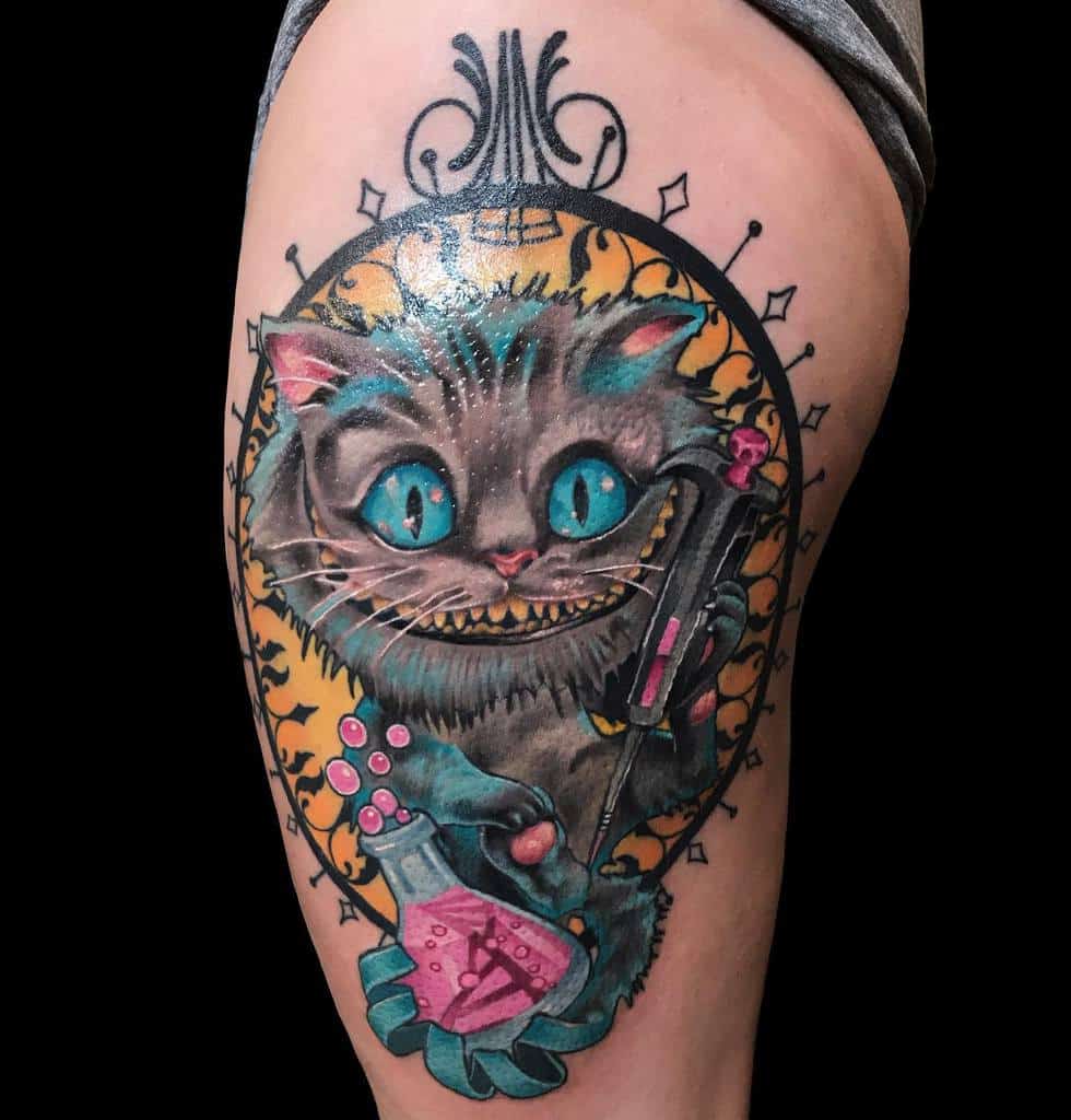 A colorful Cheshire Cat tattoo holding a key and potion bottle, framed by an ornate decorative border
