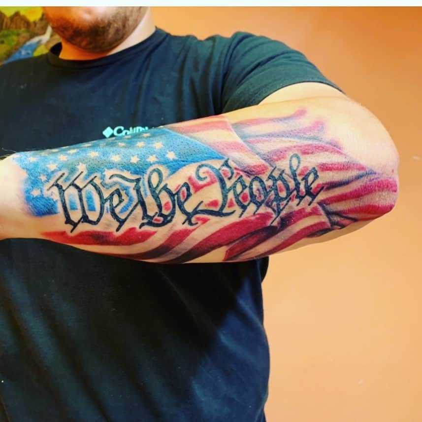 Tattooed arm with "We the People" over a waving American flag design