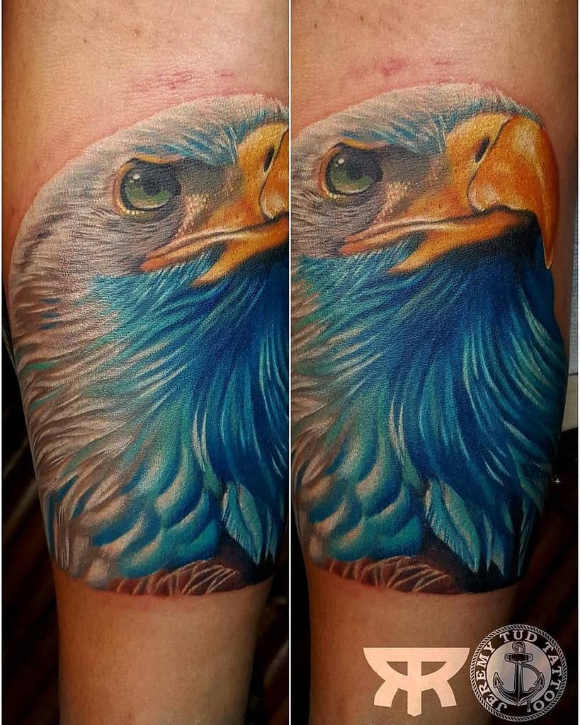 Realistic, vibrant tattoo of an eagle's head with detailed feathers and piercing eyes on an arm