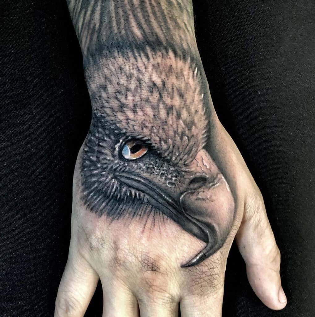 A detailed tattoo of an eagle's head, with intense eyes and a sharp beak, on the back of a hand