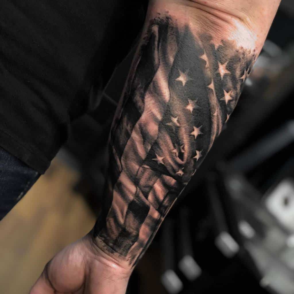 Forearm tattoo of a detailed American flag in black and gray tones