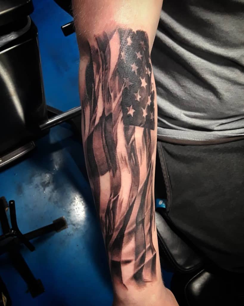 Tattoo of an American flag on a person's forearm, showcasing bold black-and-white shades