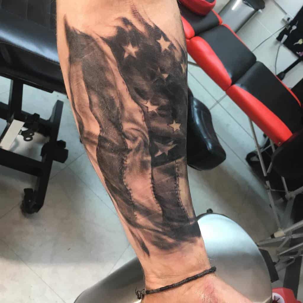 Forearm tattoo of a waving American flag in black and gray tones