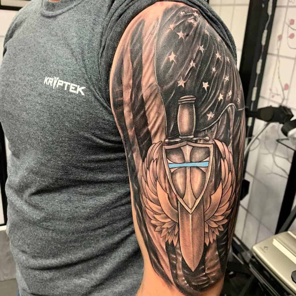 Powerful half-sleeve tattoo featuring the American flag intertwined with a bold sword and shield design, embodying strength, patriotism, and protection