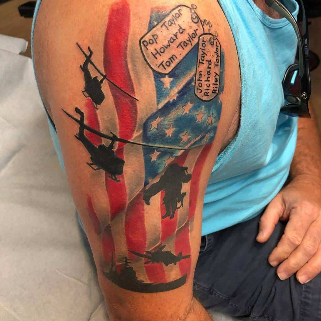 Tattoo of soldiers, helicopters, and names over an American flag background on an arm