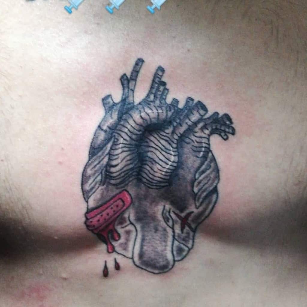 Tattoo of a bleeding human heart with a bandage and dripping blood on a person's chest