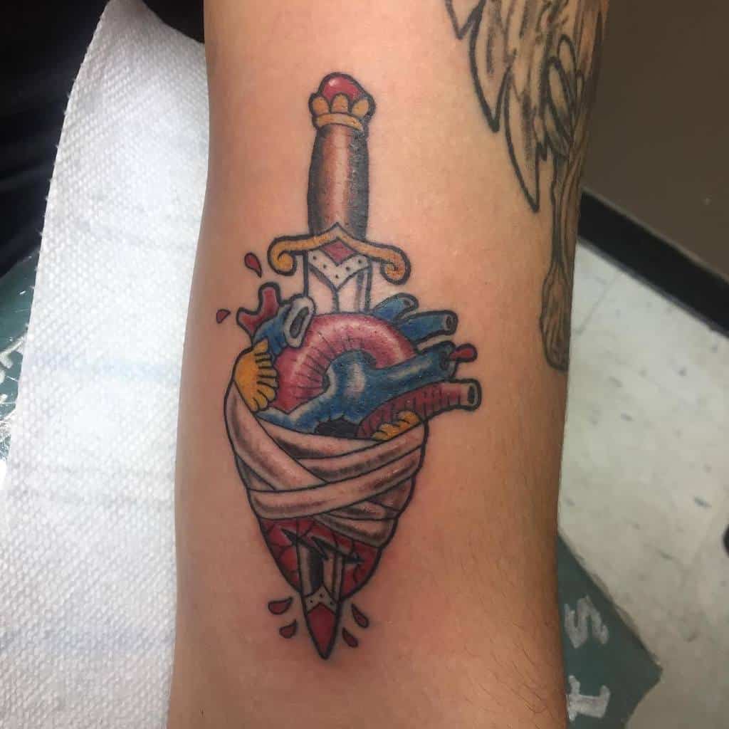 Tattoo of a bleeding dagger piercing a heart wrapped in bandages on a person's arm