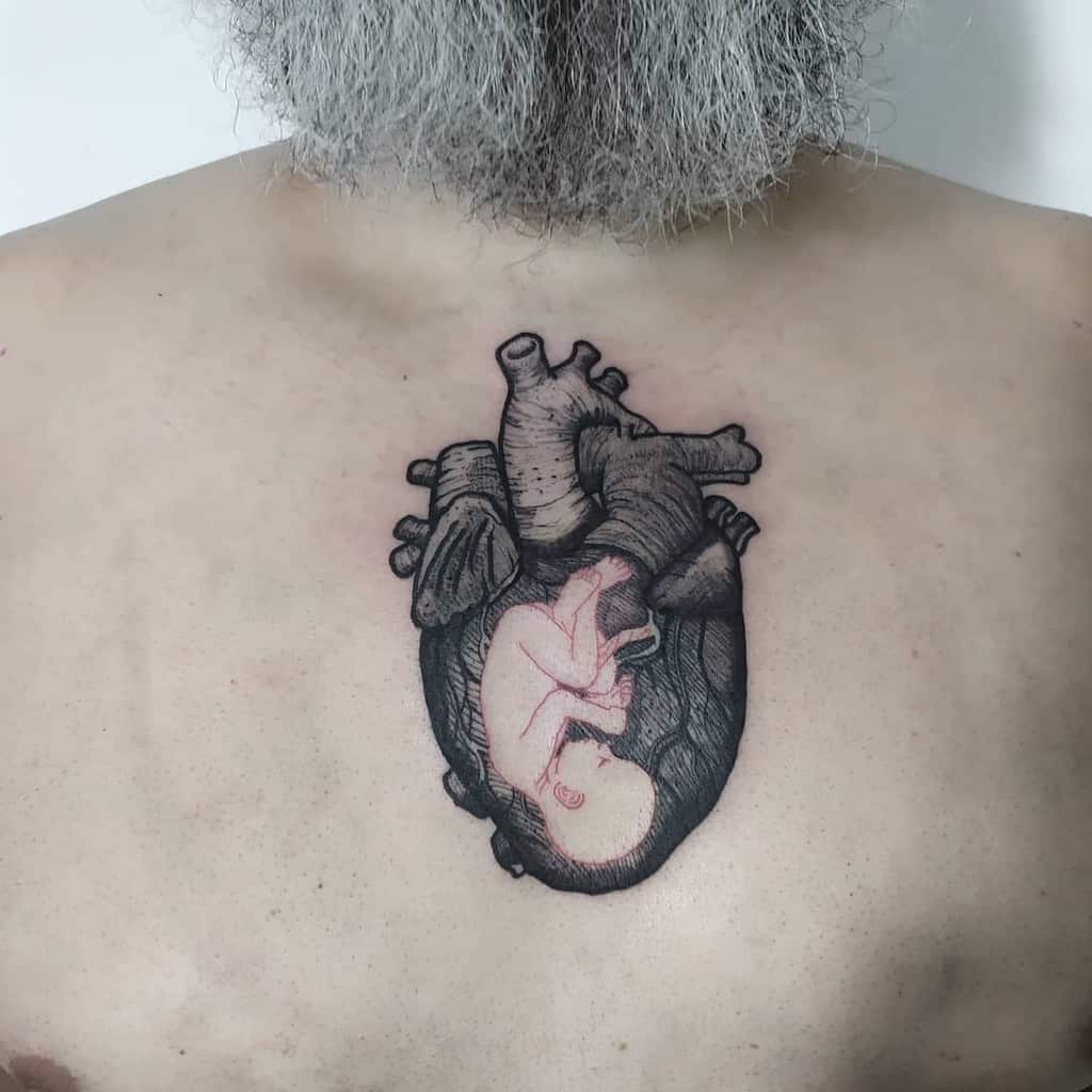 A black and grey anatomical heart tattoo with a detailed fetus inside