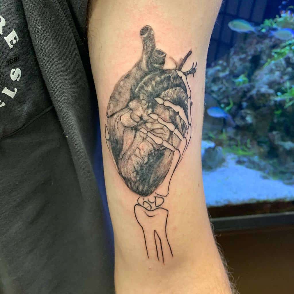 Black and grey tattoo of an anatomical heart being grasped by a skeletal hand, blending realism with fine linework
