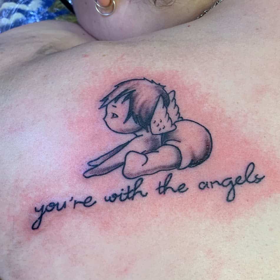 A tattoo of a baby with wings lying down with the text "you're with the angels" below it