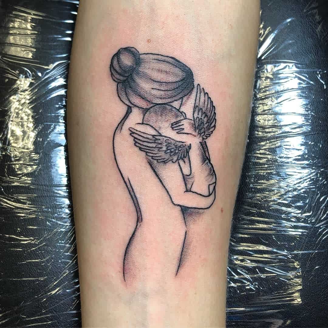 Tattoo of a woman with a bun holding a winged baby on an arm