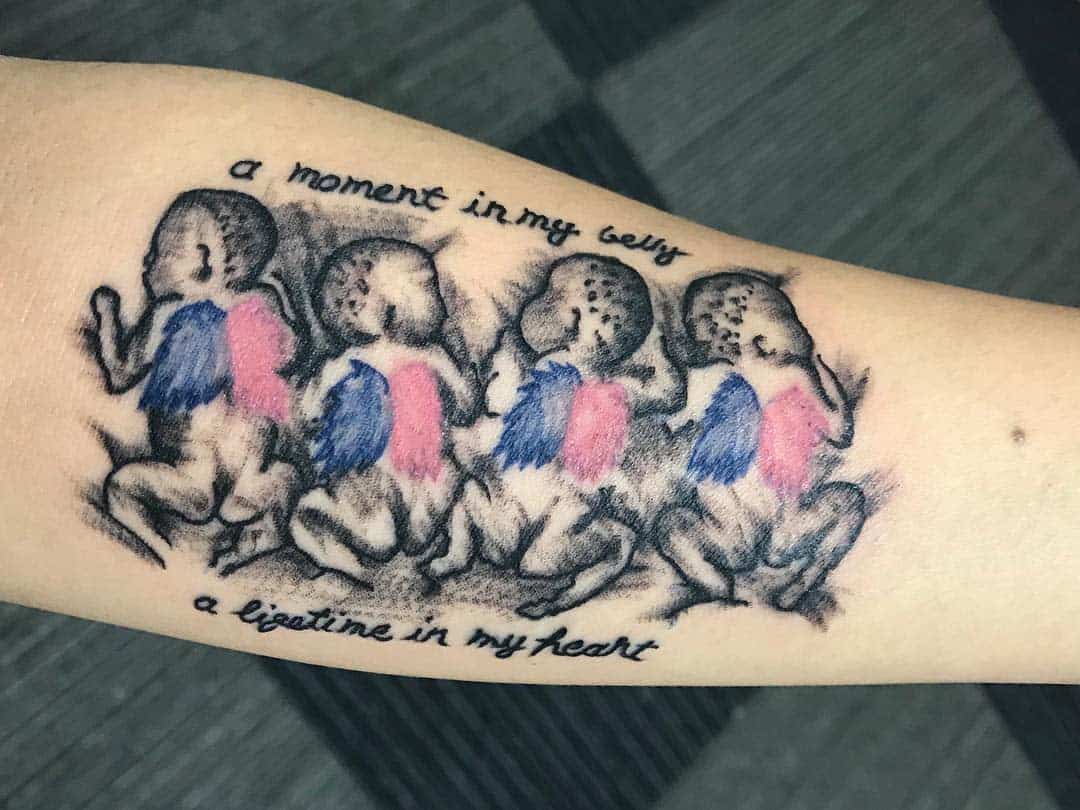 Tattoo of four babies with wings in blue and pink, accompanied by text: "a moment in my belly, a lifetime in my heart