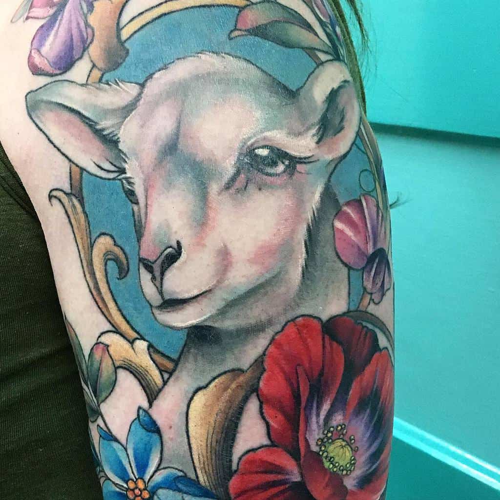 Art Nouveau-style tattoo of a serene lamb framed by flowing golden ornaments, vibrant flowers, and a soft blue mirror background