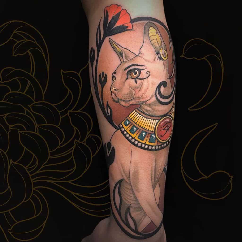 Art Nouveau-style tattoo of an Egyptian-inspired sphynx cat with golden jewelry, an Eye of Ra pendant, and flowing floral ornaments