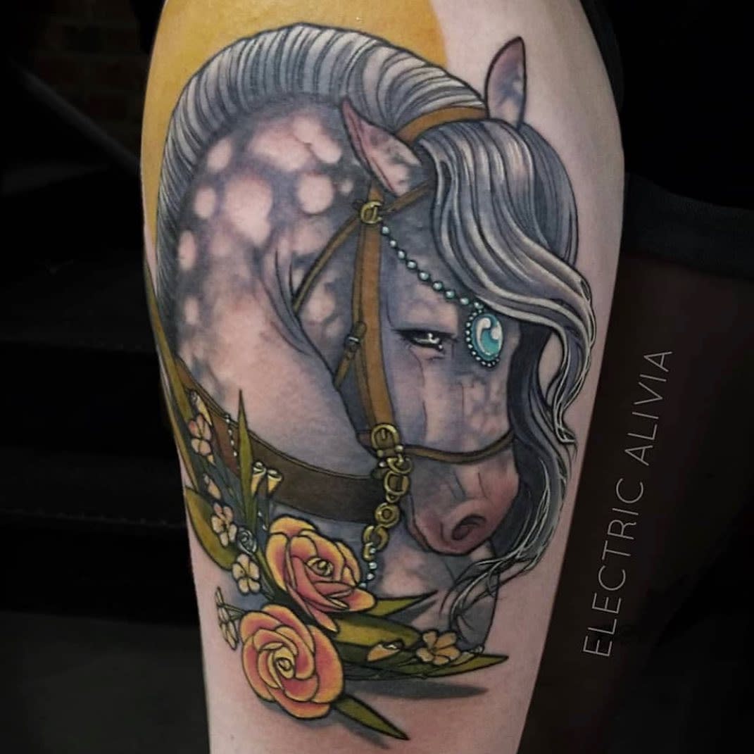 Art Nouveau-style tattoo of a majestic dappled horse with flowing mane, adorned with a blue jeweled bridle and surrounded by golden roses and green leaves