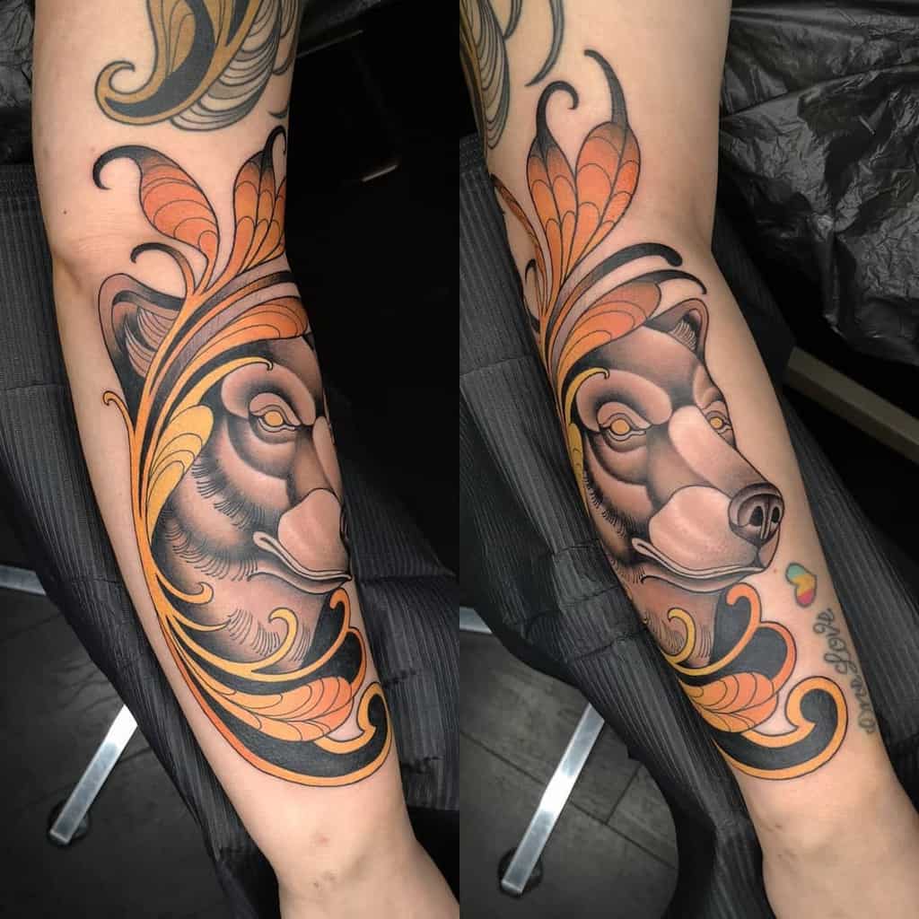 Art Nouveau-style tattoo of a wolf’s face framed by elegant flowing golden and orange ornamental leaves designs