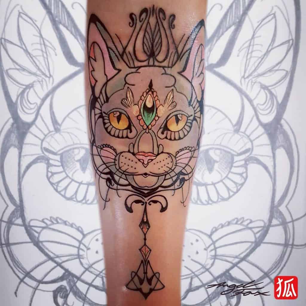 Art Nouveau-style tattoo of a mystical cat with ornate symmetrical patterns, golden eyes, a third-eye gemstone, and elegant flourishes