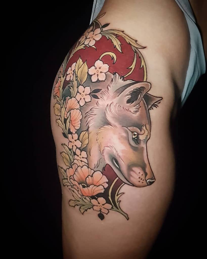 Art Nouveau-style tattoo of a wolf framed by intricate floral patterns and golden accents, set against a rich red background