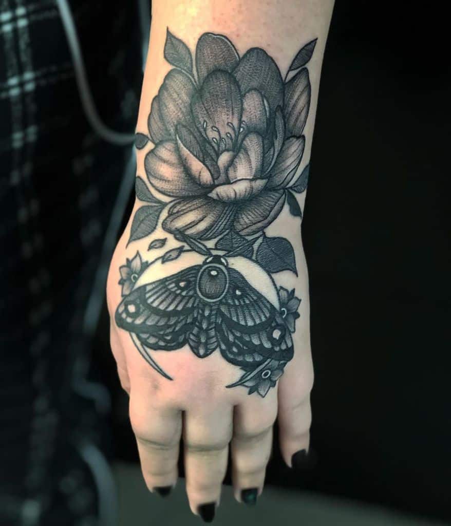 Black and grey tattoo featuring a detailed moth with floral elements and a large blooming flower