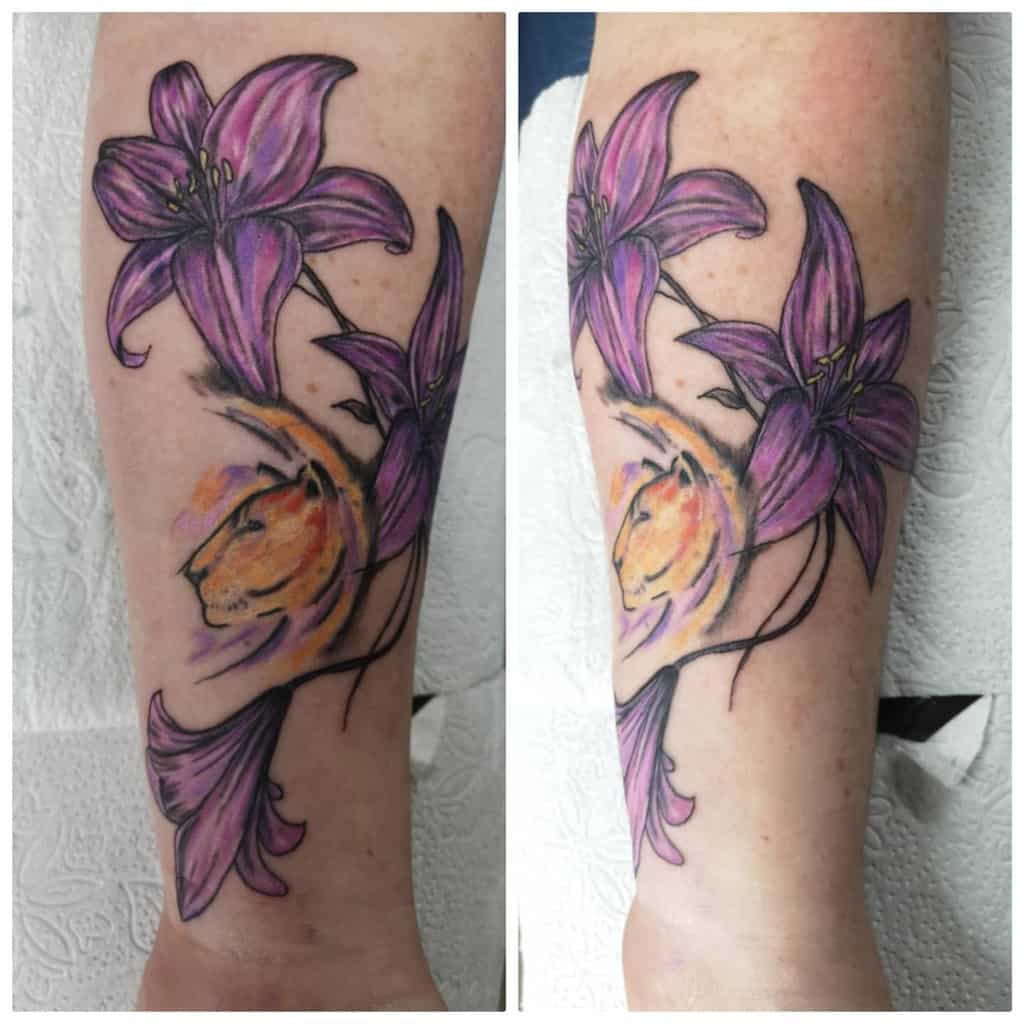 Vibrant tattoo of purple lilies with a watercolor-style lion’s face, blending floral beauty with strength and bold artistic expression