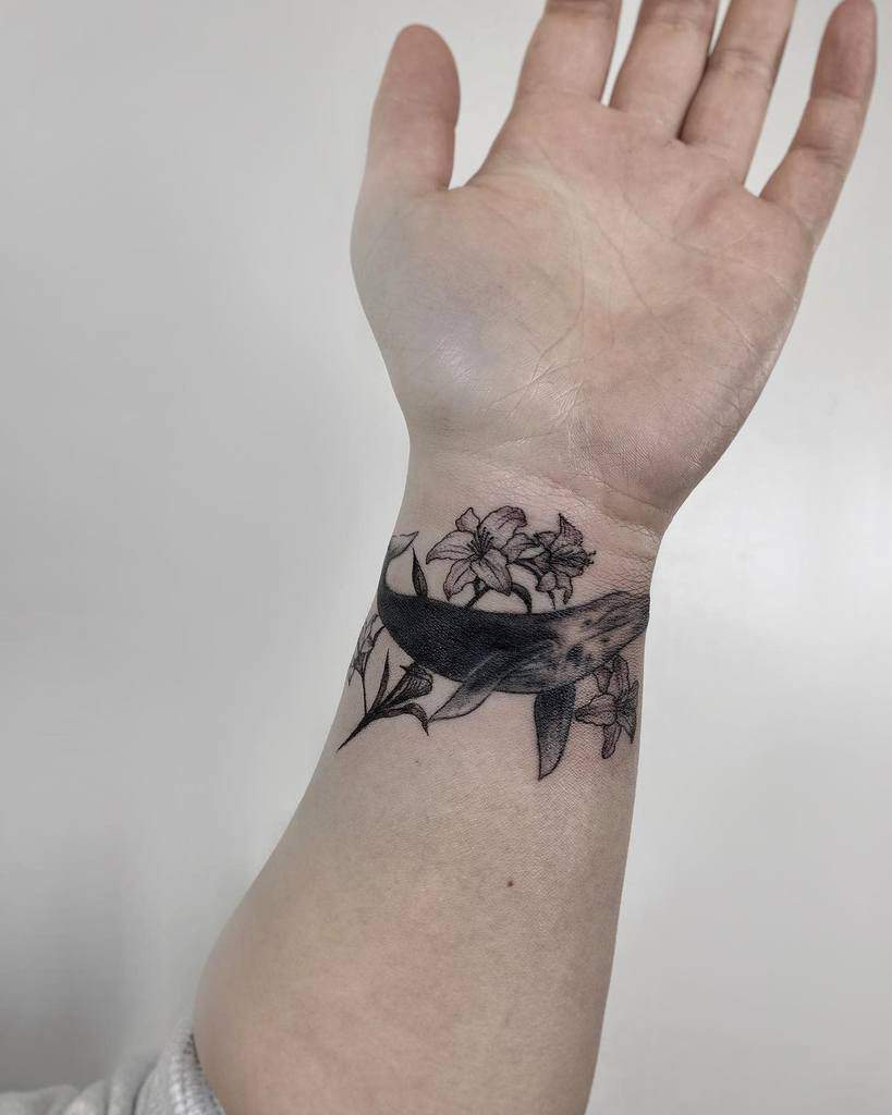 Delicate black and white tattoo of a whale swimming through lilies, blending marine and floral elements