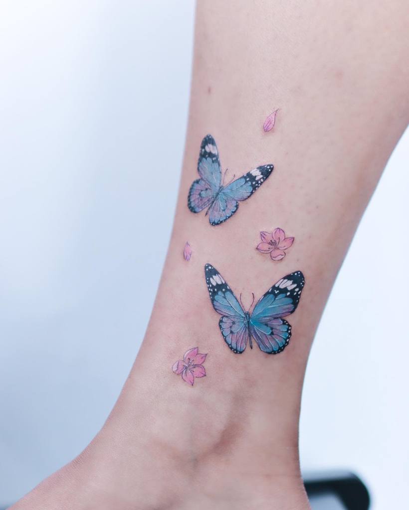A leg adorned with blue butterfly tattoos and small pink flowers around the ankle