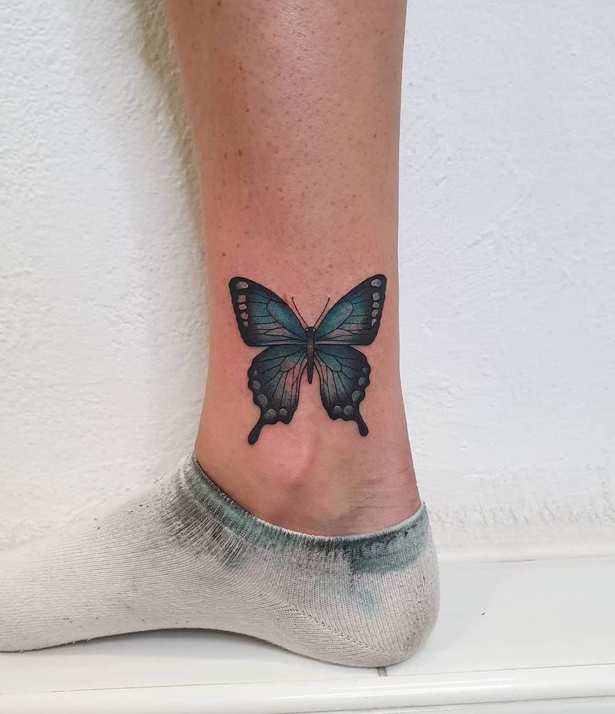 Blue and black butterfly tattoo on the inner ankle