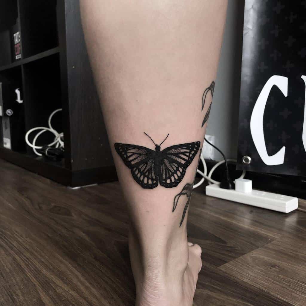 A black monarch butterfly tattoo graces the lower leg