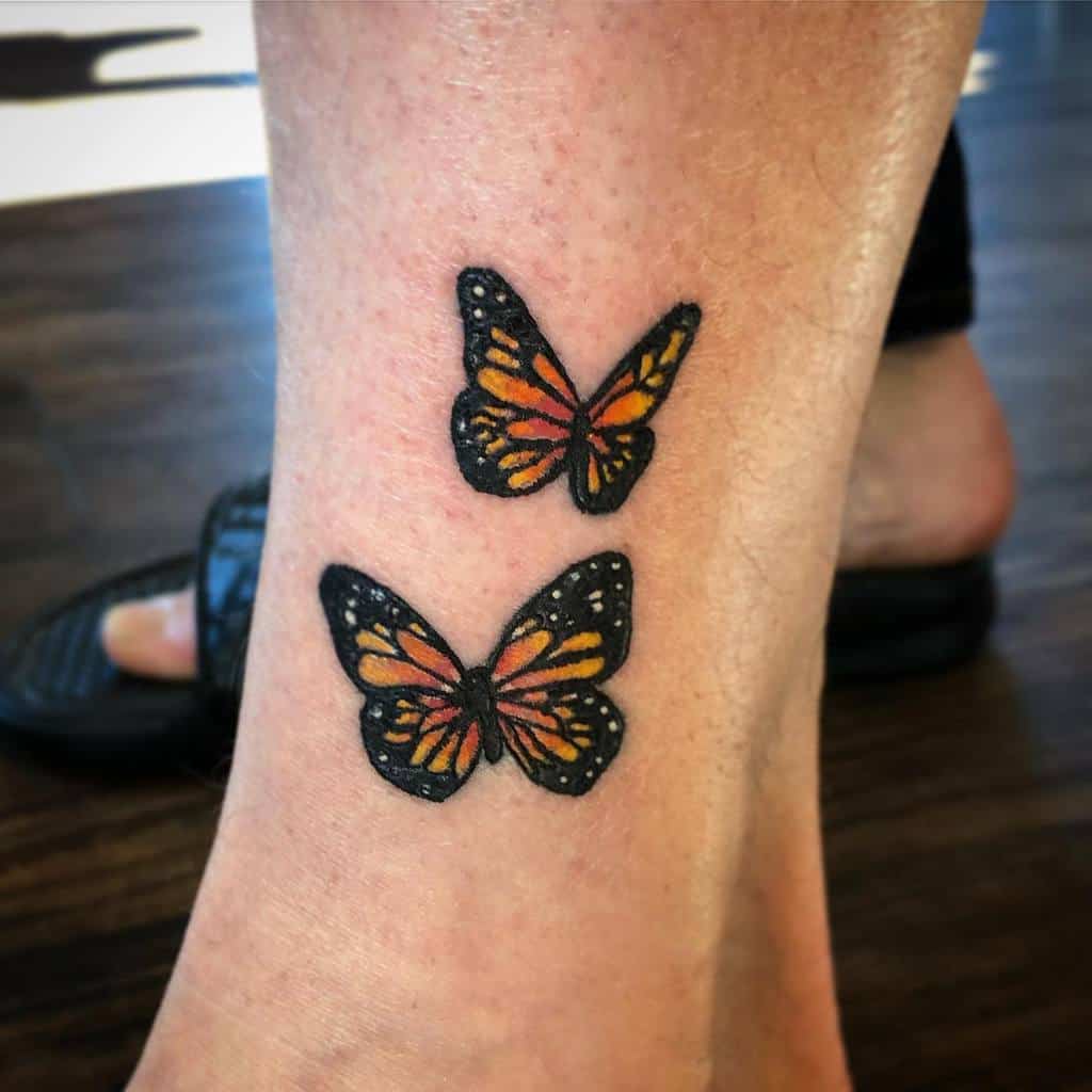 Two vibrant monarch butterfly tattoos on an ankle, showcasing intricate orange and black patterns