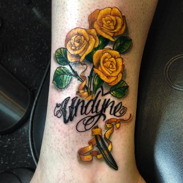 Tattoo of three yellow roses with green leaves, script "Undyne," ribbon