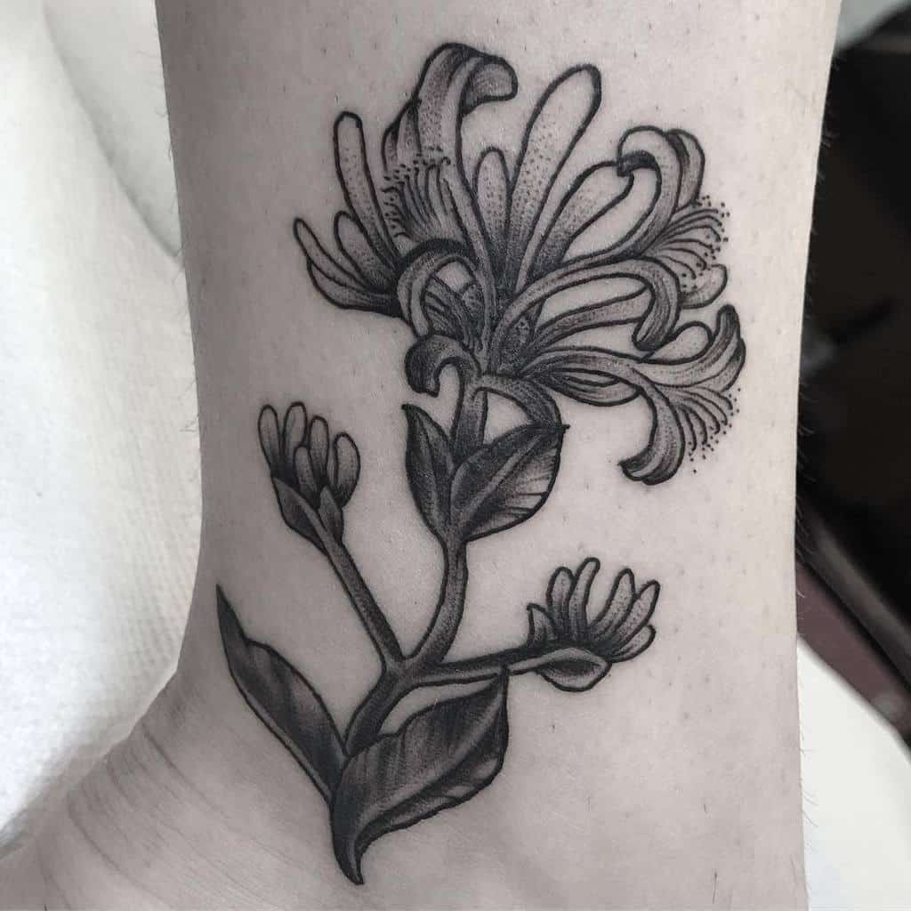 Black ink honeysuckle flower tattoo with detailed shading on the ankle, symbolizing growth