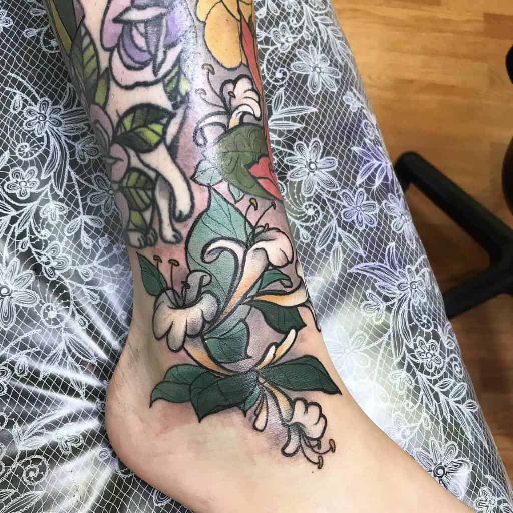 Delicate honeysuckle tattoo in soft green and white tones, wrapping gracefully around the ankle