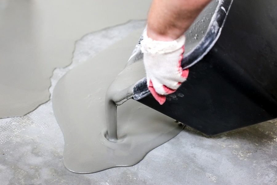 Gray epoxy floor paint being poured onto a concrete surface for leveling.