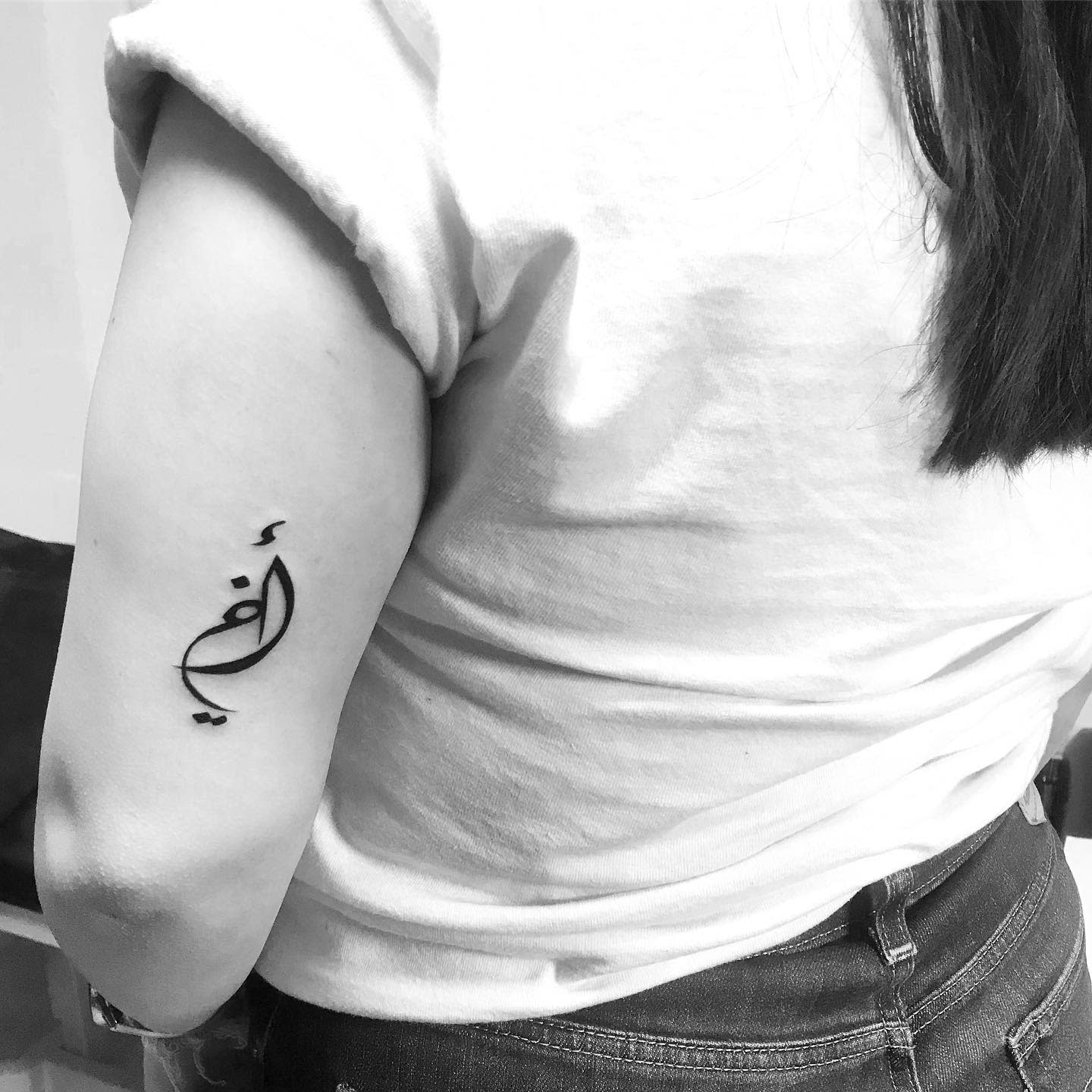 Individual with a black tattoo of Arabic script on their upper arm