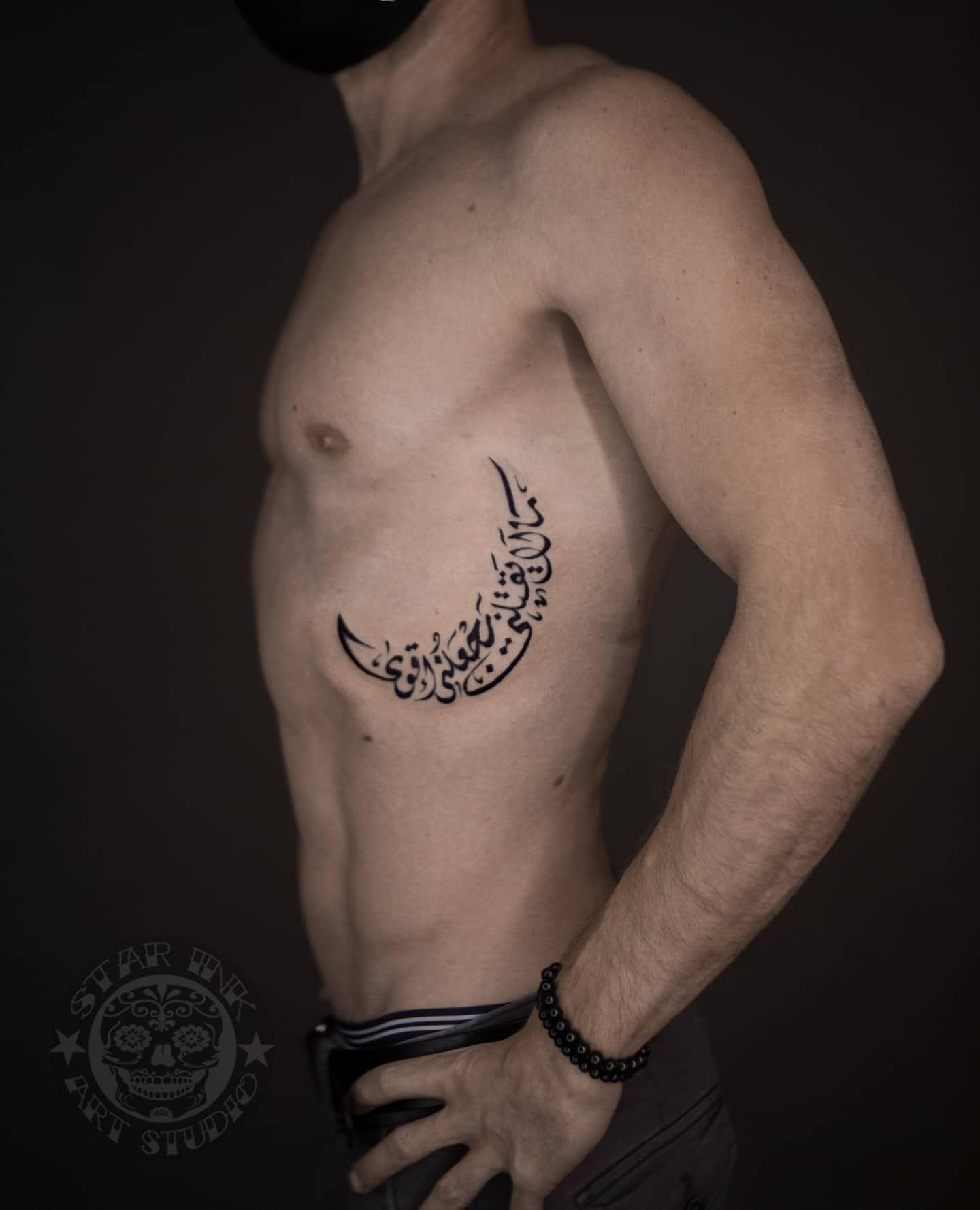 Moon-shaped tattoo and Arabic script on right ribcage