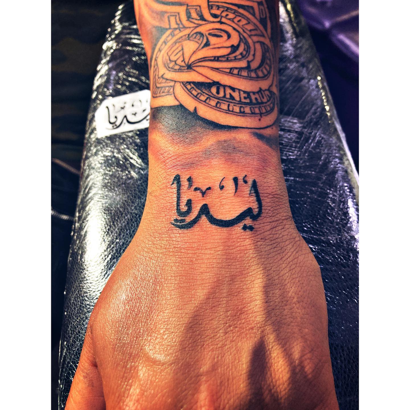 Tattooed wrist and arm featuring intricate designs and Arabic script on the inner wrist
