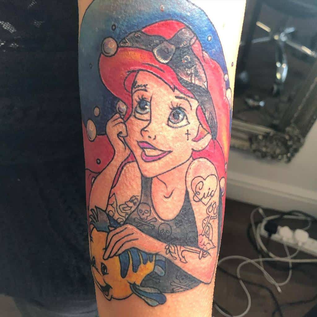 A unique tattoo of Ariel from The Little Mermaid, with modern twists like tattoos and a tank top, featuring Flounder by her side