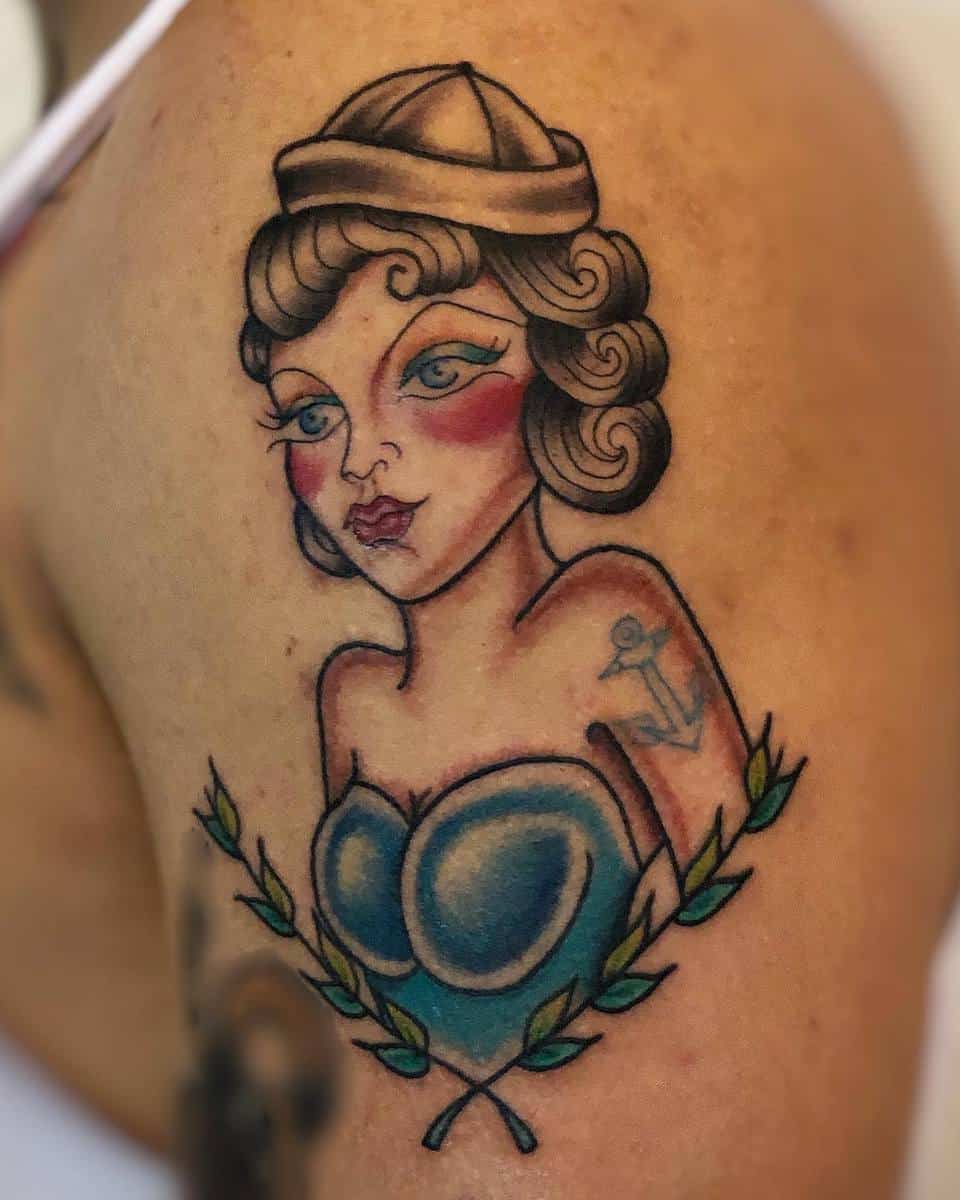 Tattoo of a vintage pin-up girl with an anchor tattoo on her shoulder and leaves at the bottom on an arm