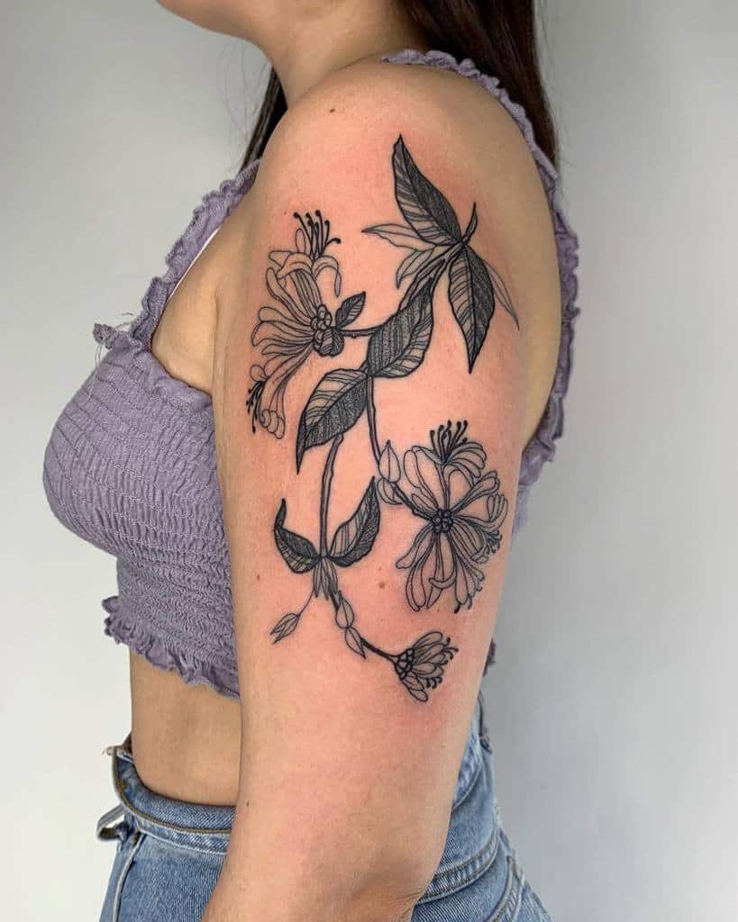 Large black ink honeysuckle tattoo on the upper arm, featuring detailed flowers and leaves