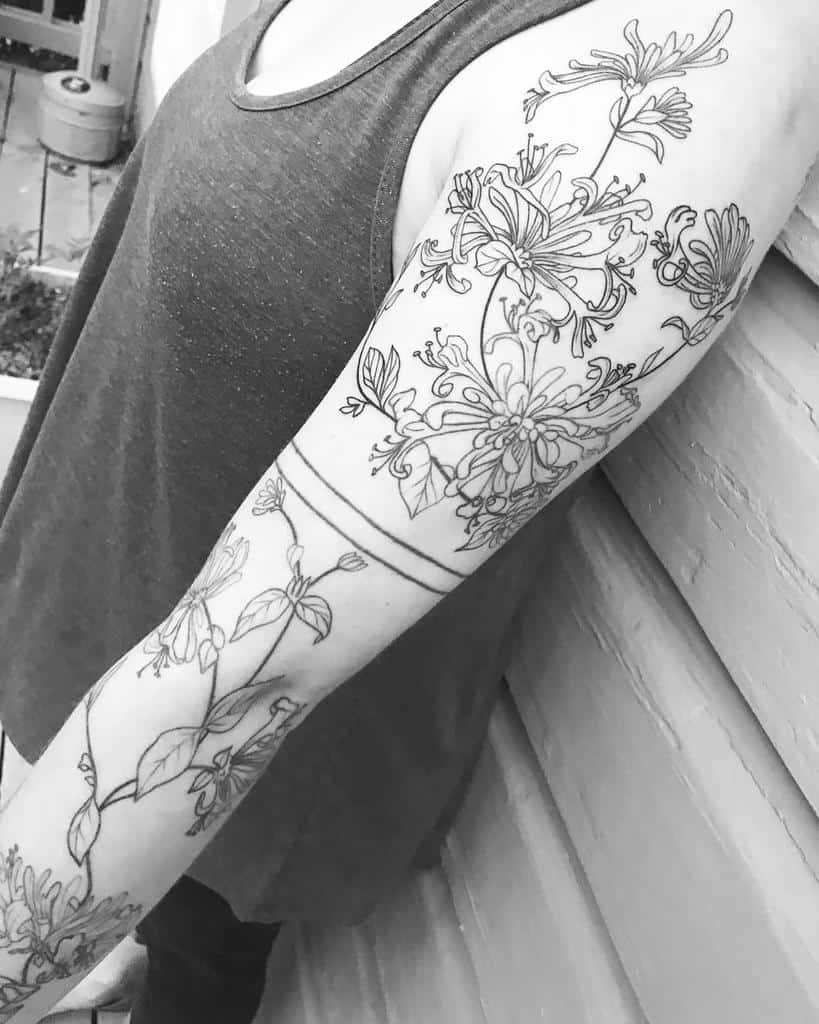 Large honeysuckle sleeve tattoo in black ink with delicate outlines covering the upper arm