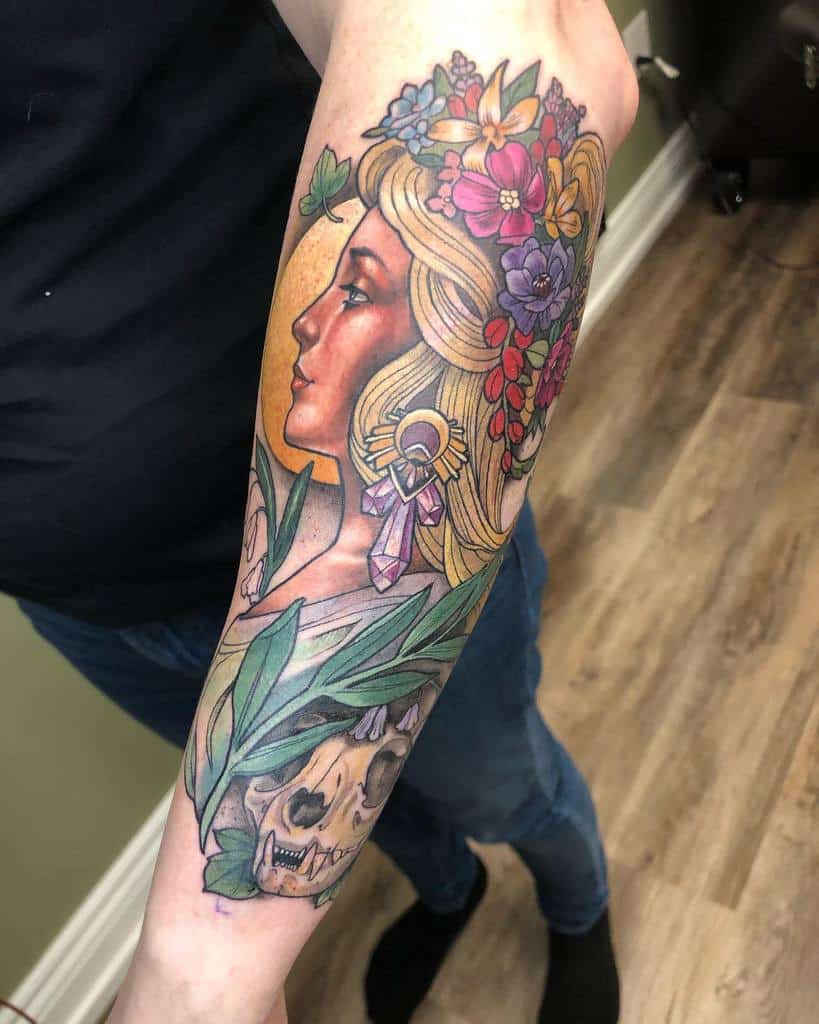 Art Nouveau-style tattoo of a woman with flowing golden hair, adorned with colorful flowers, crystals, and a wolf skull wrapped in leaves