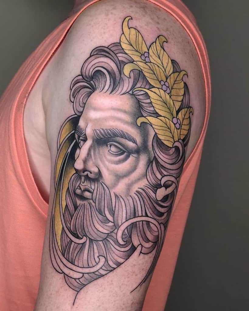 Art Nouveau-style tattoo of a bearded god-like figure with flowing hair, adorned with golden laurel leaves and intricate ornamental details
