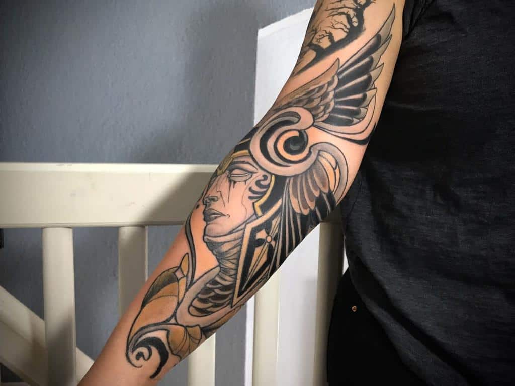 Art Nouveau-style tattoo of a winged warrior with intricate swirling designs, bold black shading, and elegant ornamental details