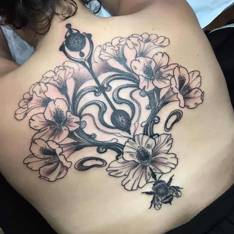 Art Nouveau-inspired back tattoo featuring flowing floral patterns, a bee, horseshoes, and ornate linework in black and gray ink